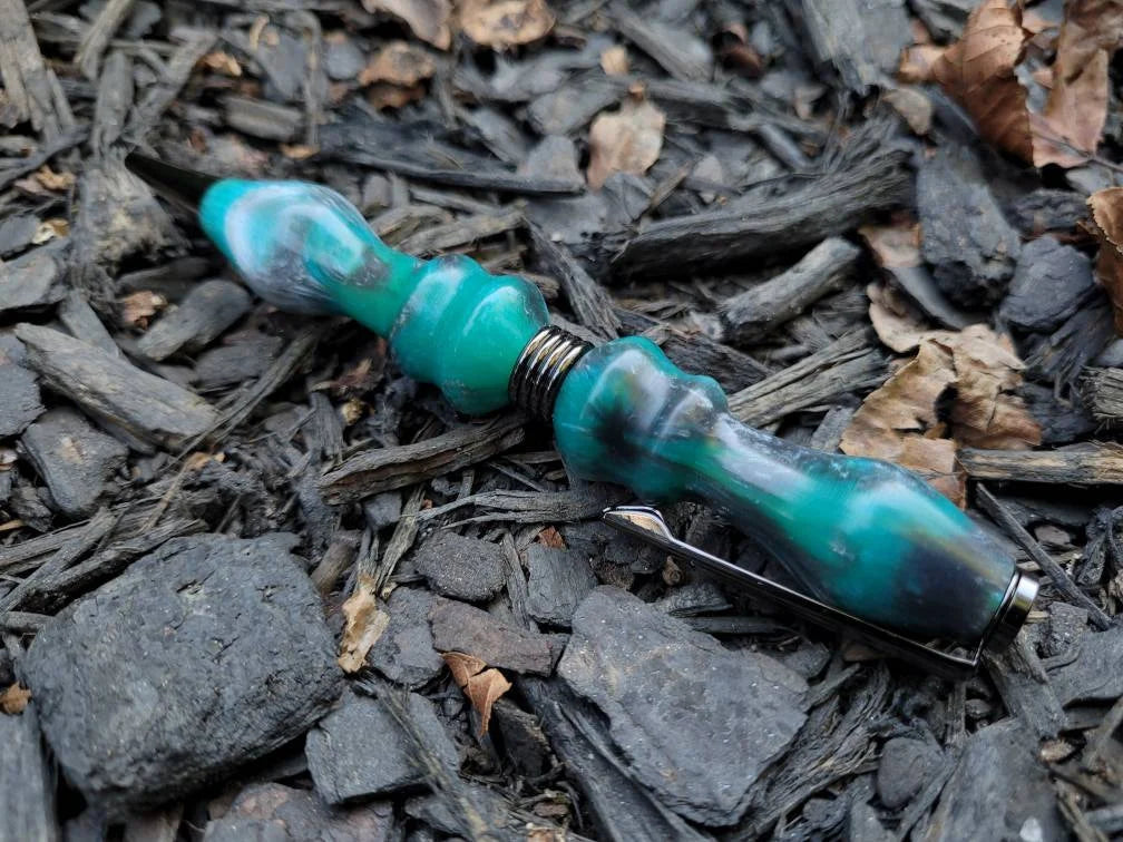Turquoise pen lying on a bed of dark soil and small rocks